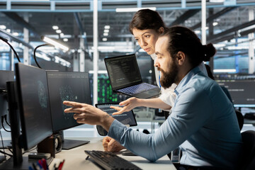 Data center manager supervising technician monitoring system performance using PC, identifying...