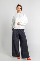 Portrait beautiful woman of model appearance. Girl in white sweatshirt, black trousers, red shoes on grey background. Pretty female with trendy makeup posing in studio. Vertical photo.