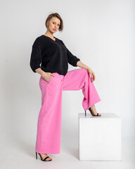 Portrait beautiful woman of model appearance. Girl in black jumper and pink trousers on grey background. Pretty female with trendy makeup posing in studio. Vertical photo. 