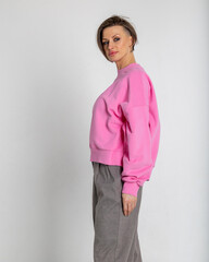 Portrait beautiful woman of model appearance. Girl in pink sweatshirt, grey trousers on grey background. Pretty female with trendy makeup posing in studio. Vertical photo.