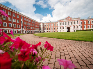 Red flowers in foreground and huge court yard of Jelgava palace with well looked after grass lawn...