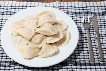 A plate of dumplings sits on a checkered cloth. The dumplings are white and arranged in a neat pile, Popular East European food. Simple easy meal.