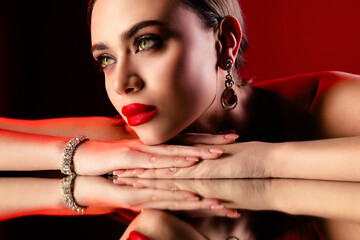 Stunning woman in red dress with glamorous jewelry posing in dramatic lighting for a sophisticated...
