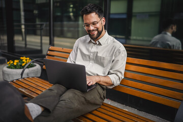 Adult man tourist passenger sit on bench at street and use laptop