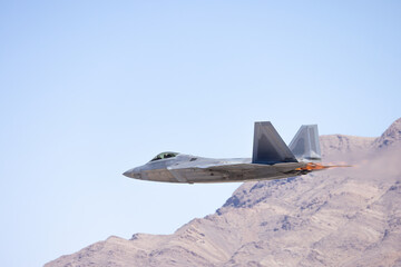 Extremely close  side view of a  F-22 Raptor  against the Nevada hills, with afterburners on.