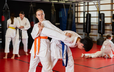 Teenage boy and girl in kimonos train judo techniques in group in studio