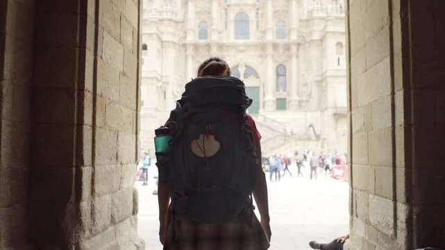 Middle-aged backpacker woman pilgrim entering Obradoiro square. rising hands in Santiago de Compostela, Spain with Santiago de Compostela Cathedral &mdash; famous Camino de Santiago finish point 4K footage