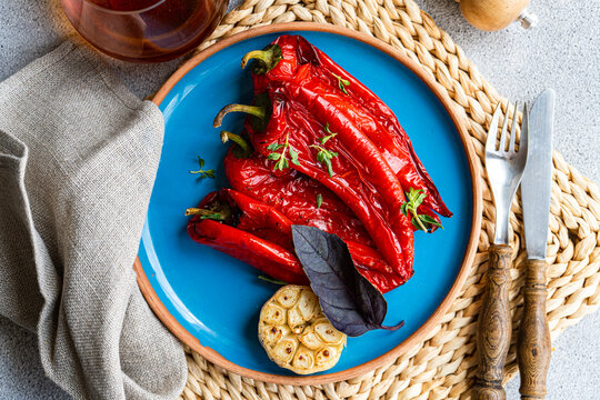 Close-up overhead view of roasted red bell peppers with garlic and a glass of wine on a table