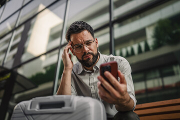 Worried businessman have a headache and use cellphone on bench