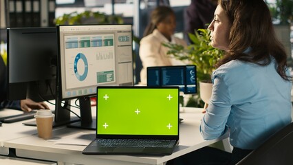 Green screen mockup laptop next to accountant inputting financial figures on PC after checking...