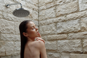 woman showering in bathroom, wet hair, relaxing under rain showerhead, natural stone wall...