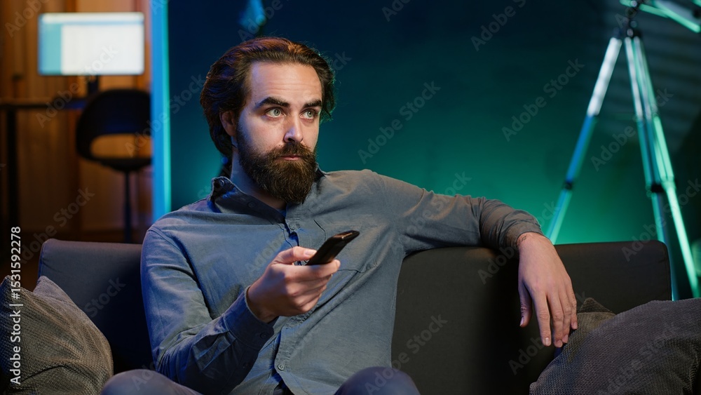 Poster man sitting on couch browsing though movies available on streaming service, enjoying time off from w