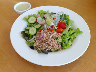 Tuna salad and vegetables food on a white plate and salad dressing in a cup on the table, food, copy space