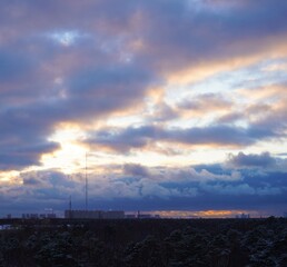 Sunset over the city skyline with a TV tower.
winter sunset with thick clouds and bright rays of light against the backdrop of the city panorama. A TV tower, a forest and tall houses are visible.