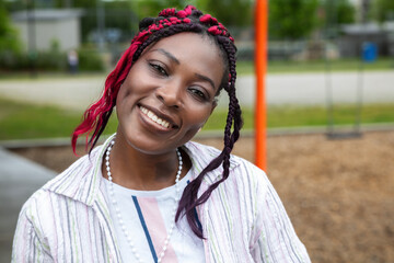 Happy African American daycare teacher smiling at outdoor playground during work break