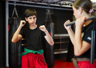 Naklejka premium Teenage boy and girl train karate techniques training with nunchucks in studio