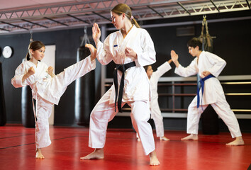 Boy and girl in kimonos train karate techniques with young woman coach in studio