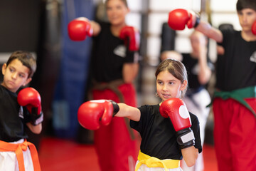 Group of children in boxing gloves are training in gym, repeatedly repeating punches, following...