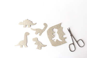 Prehistoric dinosaur silhouettes and scissors on white surface during diy process, great for homeschool tools, craft kit branding, classroom visuals, children book illustration concepts, © Elena