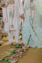 Wedding ceremony: couple holding hands, adorned with garlands, stepping over flowers in traditional attire. Celebration of love and commitment.