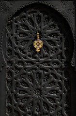 Morocco, Marrakesh. Typical old arabesque black wooden door with brass door-knock. Symmetrical Islamic pattern.