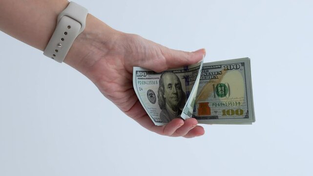 A hand holding several hundred dollar bills against white background. The scene is minimalistic and simple, finance, shopping, and consumerism concepts