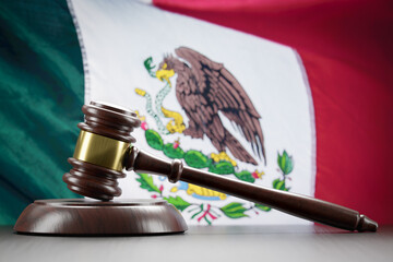Wooden Gavel Resting on Table In Front of Mexican Flag.