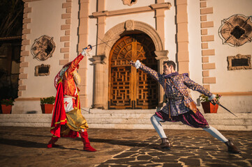 Spanish men in traditional colonial clothing dueling with swords called foils and daggers in a traditional 1600s town setting.