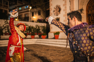 Spanish men in traditional colonial clothing dueling with swords called foils and daggers in a traditional 1600s town setting.