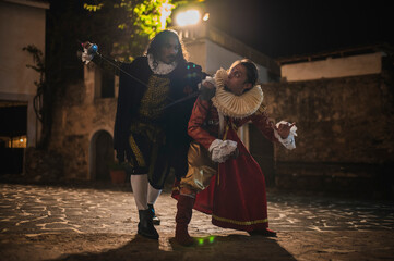 Spanish men in traditional colonial clothing dueling with swords called foils and daggers in a traditional 1600s town setting.
