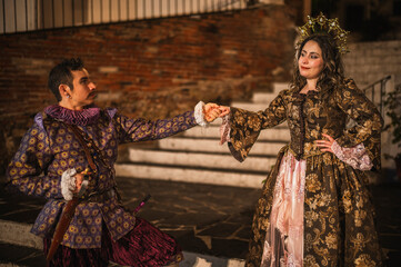 A flirting couple from the Spanish Colonial era, a man in a traditional Spanish suit dressed in purple and pink, and a girl with a princess-style tiara in a beautiful dress.