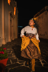 Brunette girl wearing 1600s Spanish colonial clothing running through colonial streets at night.