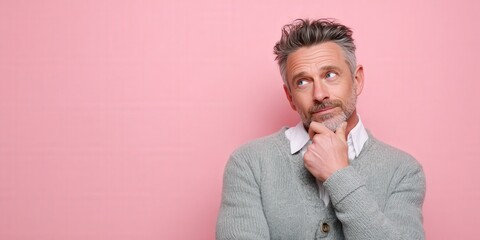 Thoughtful Man in Gray Sweater Against Pink Background