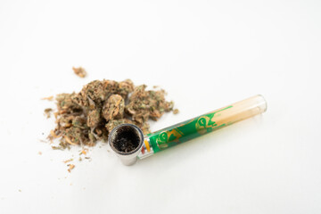 Cannabis lies next to bong on white background, preparing for consumption. This setup highlights...