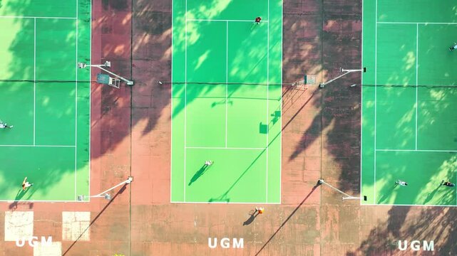 Aerial View of Three Tennis Courts with Players Engaging in a Game at UGM