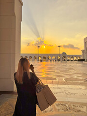 A female tourist is standing in front of the Abu Dhabi presidential palace, taking a photo at...