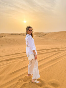 Woman standing on sand dunes in the desert at sunset, looking back over her shoulder at camera.