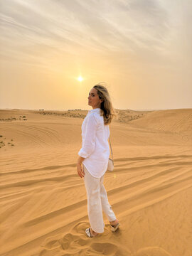 Woman standing on sand dunes in the desert at sunset, looking back over her shoulder.