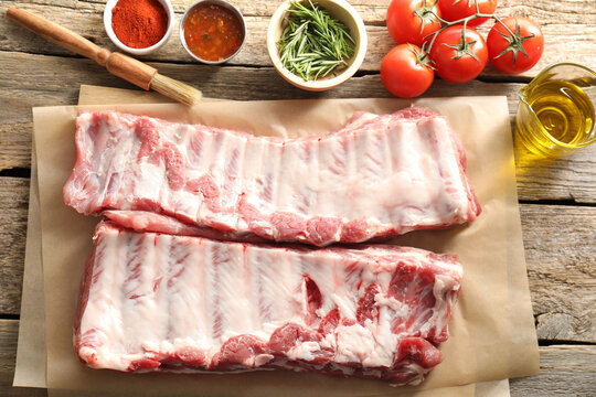 Raw pork ribs, spices and tomatoes on wooden table, flat lay