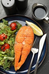 Seafood. Tasty salmon steak served with salad and lemon on black table, flat lay