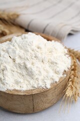 Wheat flour and spikes on white table, closeup