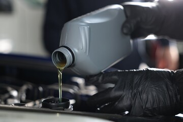 Worker pouring motor oil from canister into car engine, closeup