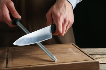 Man sharpening knife with sharpener on wooden table, closeup