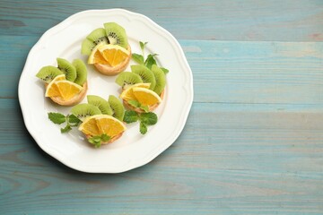 Delicious dessert. Tartlets with fruits and mint on light blue wooden table, top view. Space for text