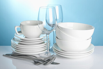 Different clean dishes on white table against light blue background