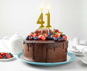 Yummy chocolate cake with fruits and burning number shaped candles on white table. 41th birthday or...