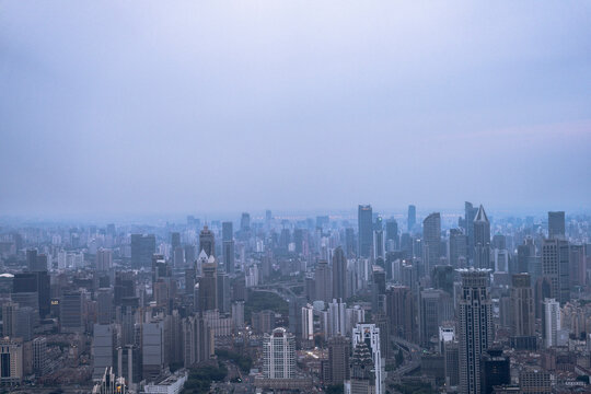 Aerial view of Shanghai city skyline under cloudy evening sky, showing dense high-rise buildings and sprawling urban layout.