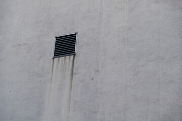 A ventilation shaft with a grille in front of it on a house wall
