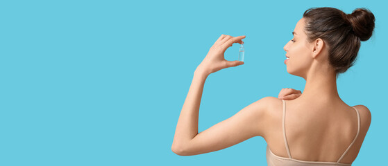 Beautiful young woman holding ampoule on blue background with space for text. Cosmetology concept