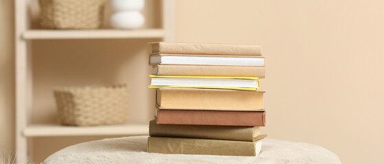 Stack of books on pouf and rack with decor near color wall